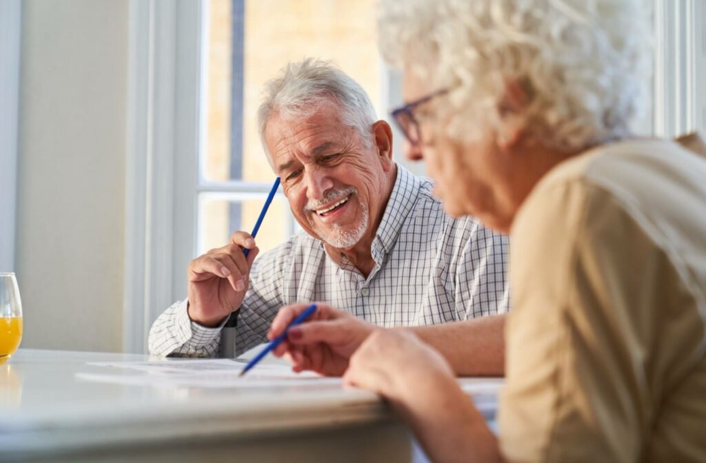 Two smiling older adults sitting at a table with paper and pens, discussing their care options.