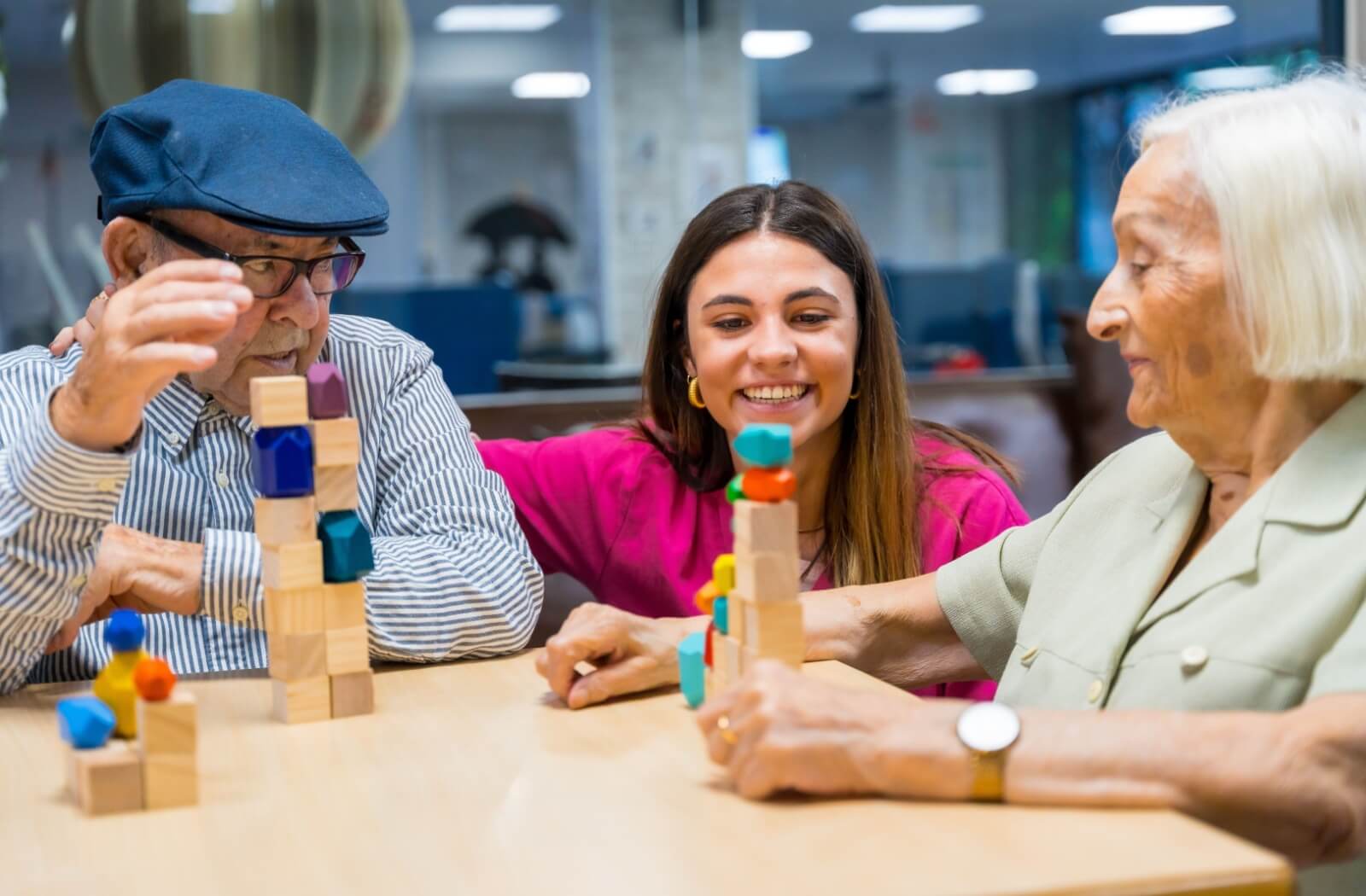 A smiling nurse helps two memory care residents with a puzzle game.