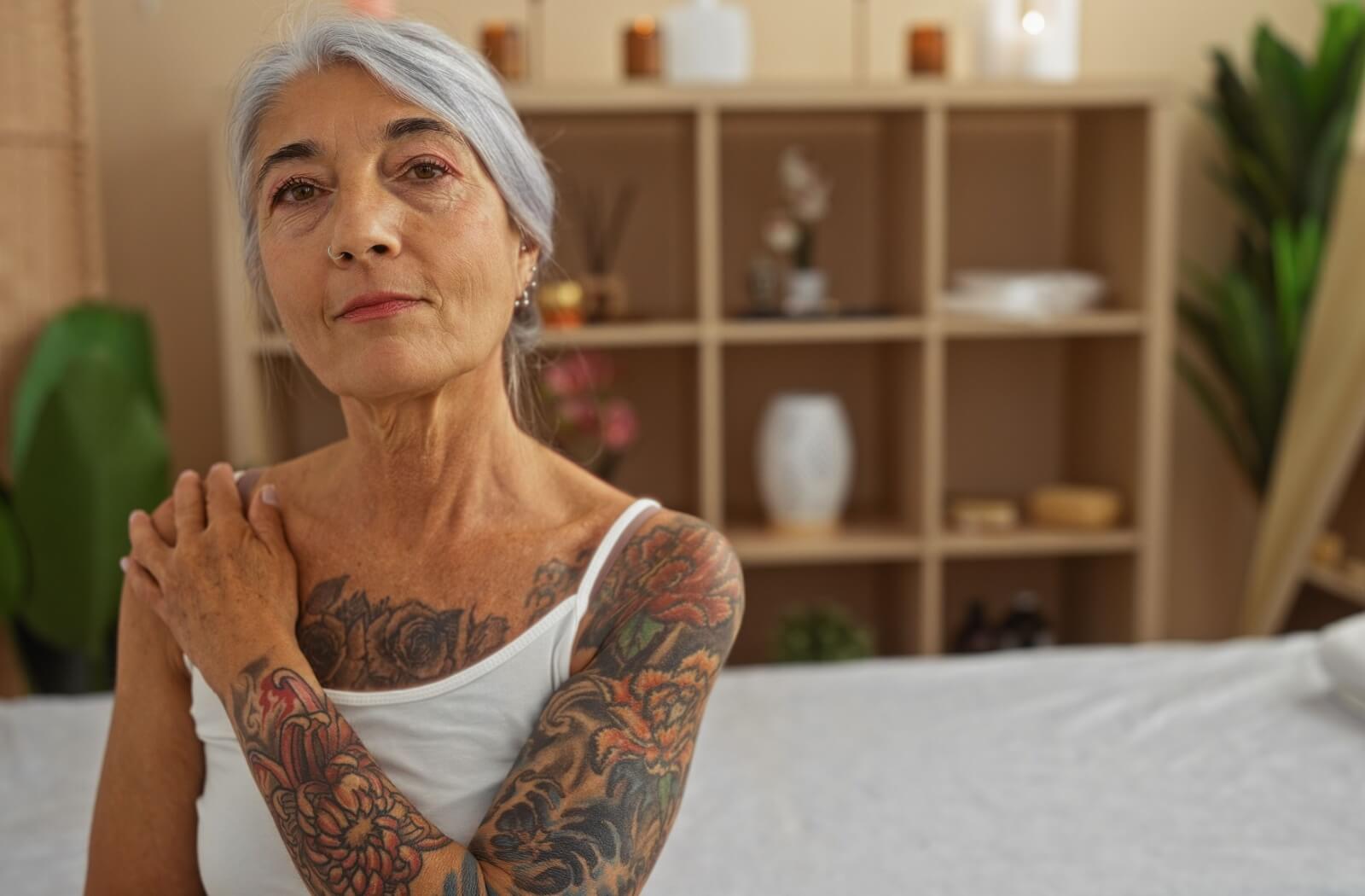 A senior wearing a white shirt with a large arm tattoo and a floral chest displays their tattoos proudly.