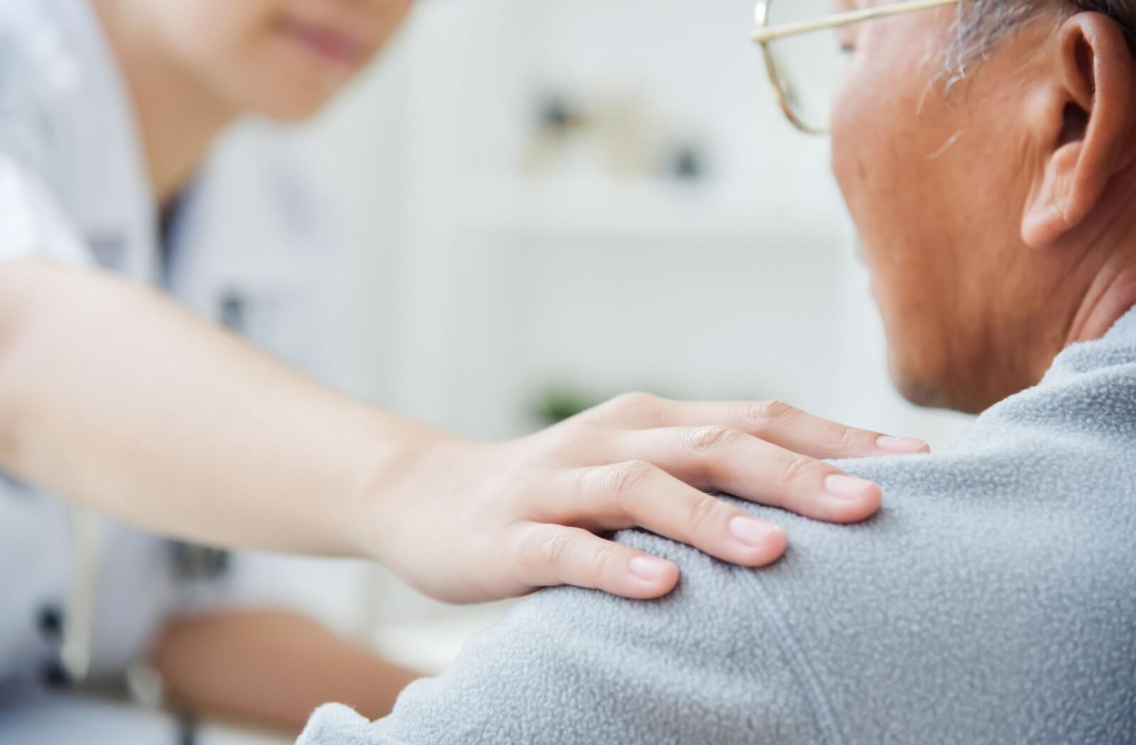 A caregiver gently touching an older adult's shoulder to reassure them during a health checkup.