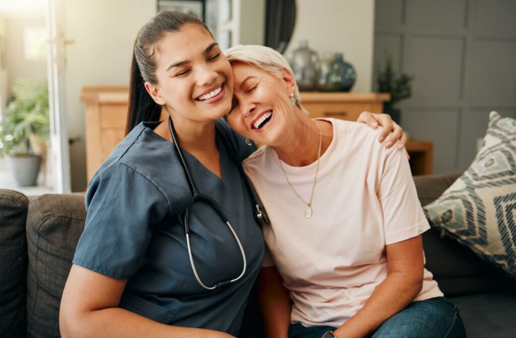An older adult leaning on the shoulder of a caregiver in senior living and laughing.