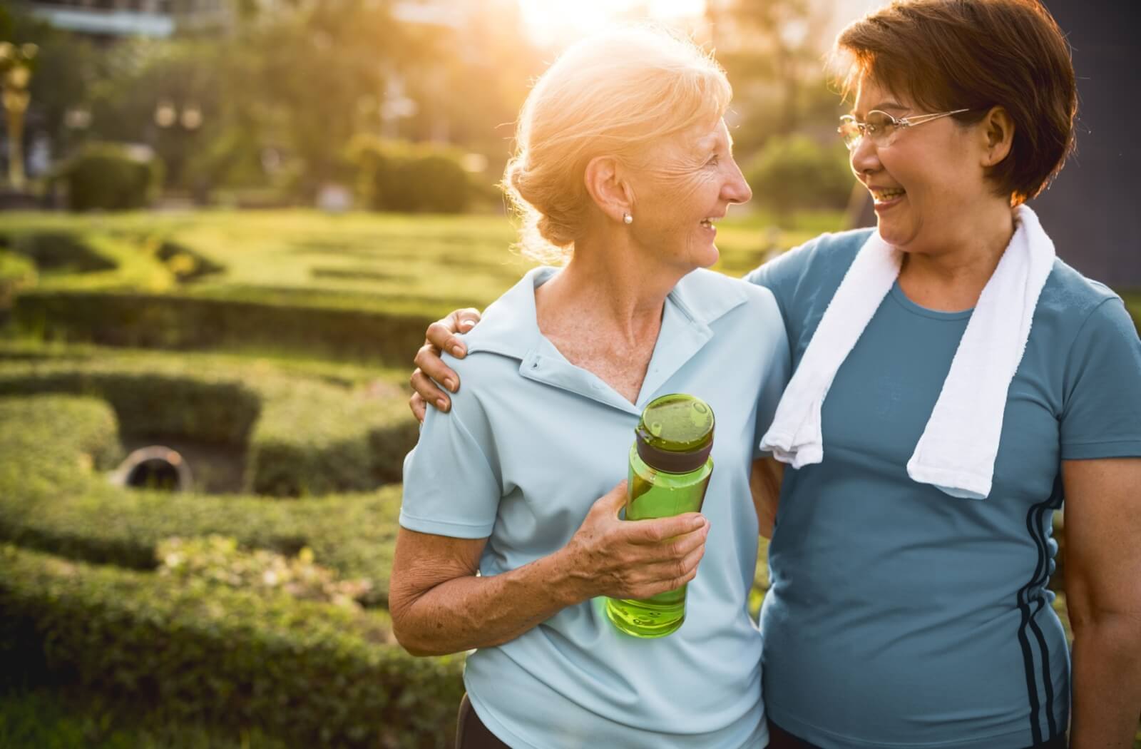 Two seniors hug and smile at each other while out for a morning walk near their senior living community.